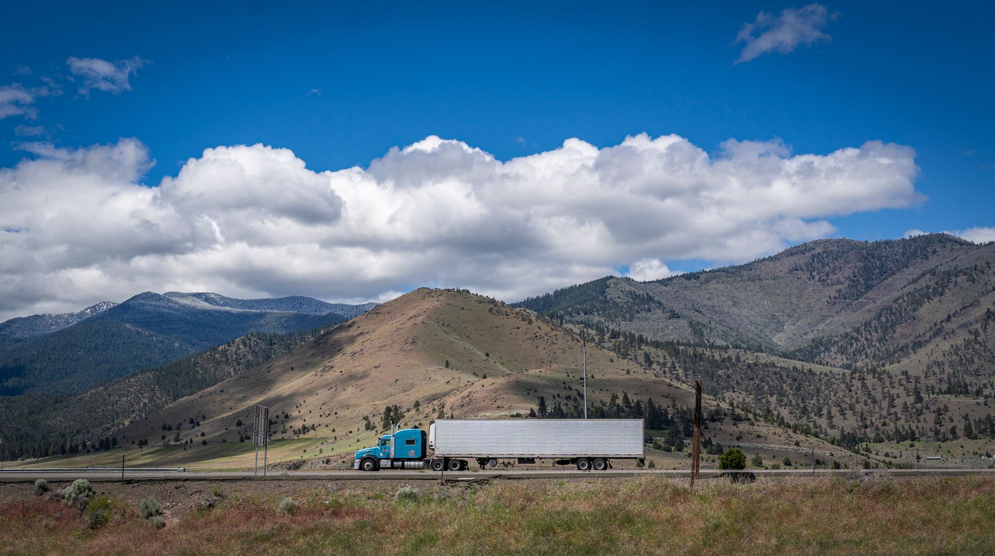 Illustrative industry photograph of a semi truck traveling beneath a mountain range